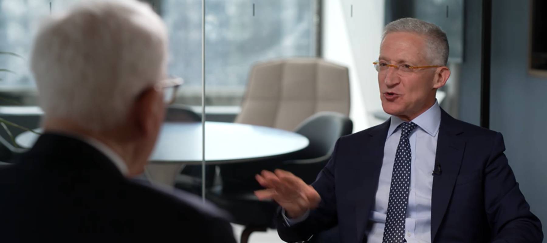 Two men sitting in an office, facing each other and engaging in a heated discussion.