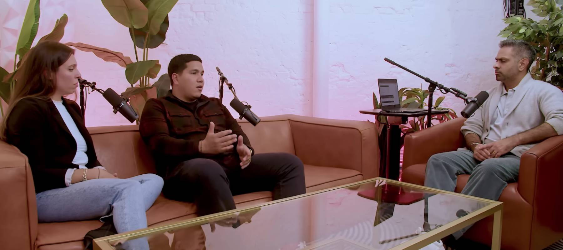 Two people sitting on a couch, talking to man in chair. Podcast living room setting.