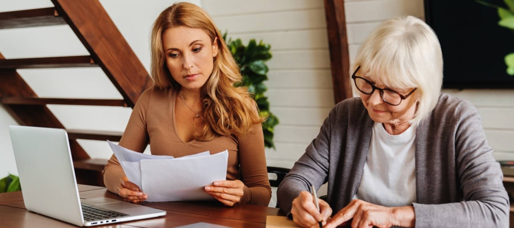 senior woman with help of her daughter making bills at home, paying loan, debt, filling in medical insurance, etc.