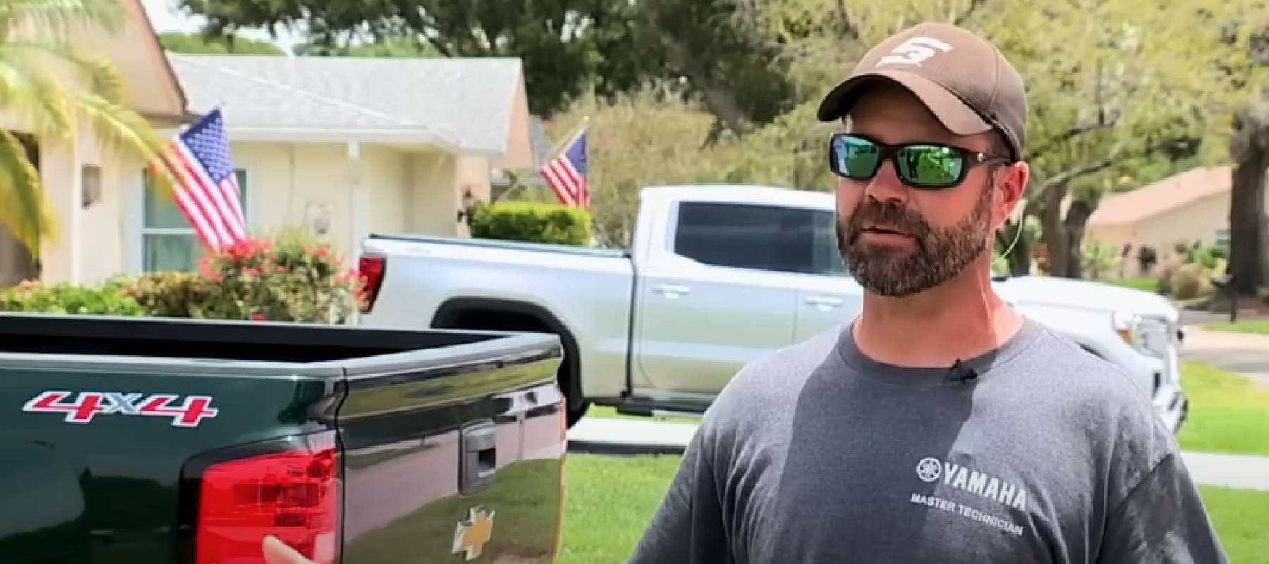 Man in sunglasses and hat stands in driveway in front of pickup truck.