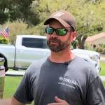 Man in sunglasses and hat stands in driveway in front of pickup truck.