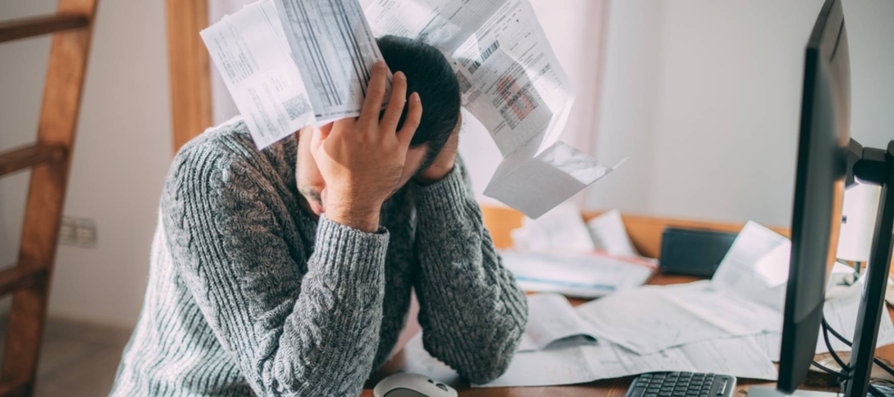 upset man in a warm sweater is sitting at a table with utility bills in his hands