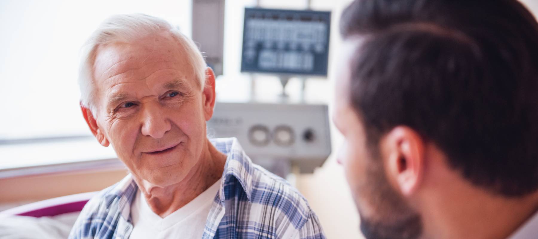 Handsome old man is talking with a doctor while sitting in hospital ward