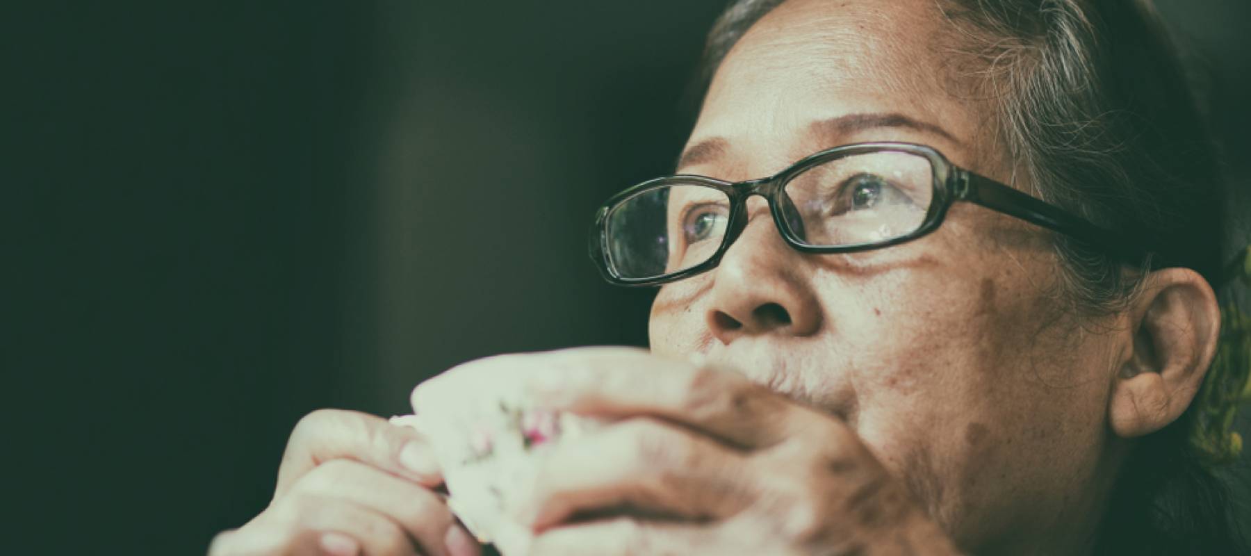 Asian elderly woman having tea and looking outside