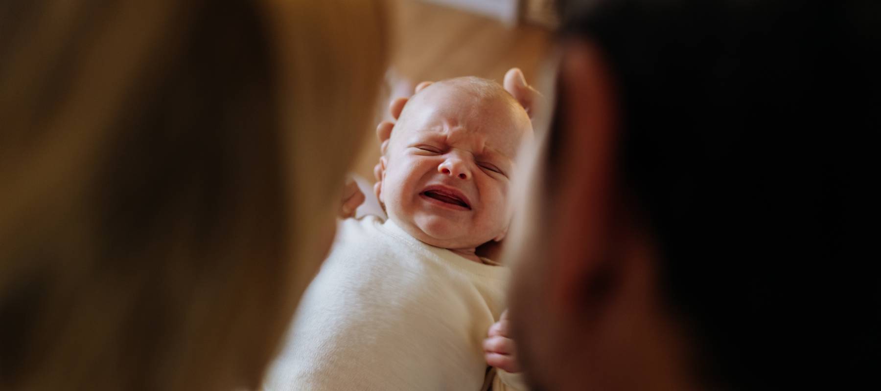 Close up over shoulder of parents holding crying baby.