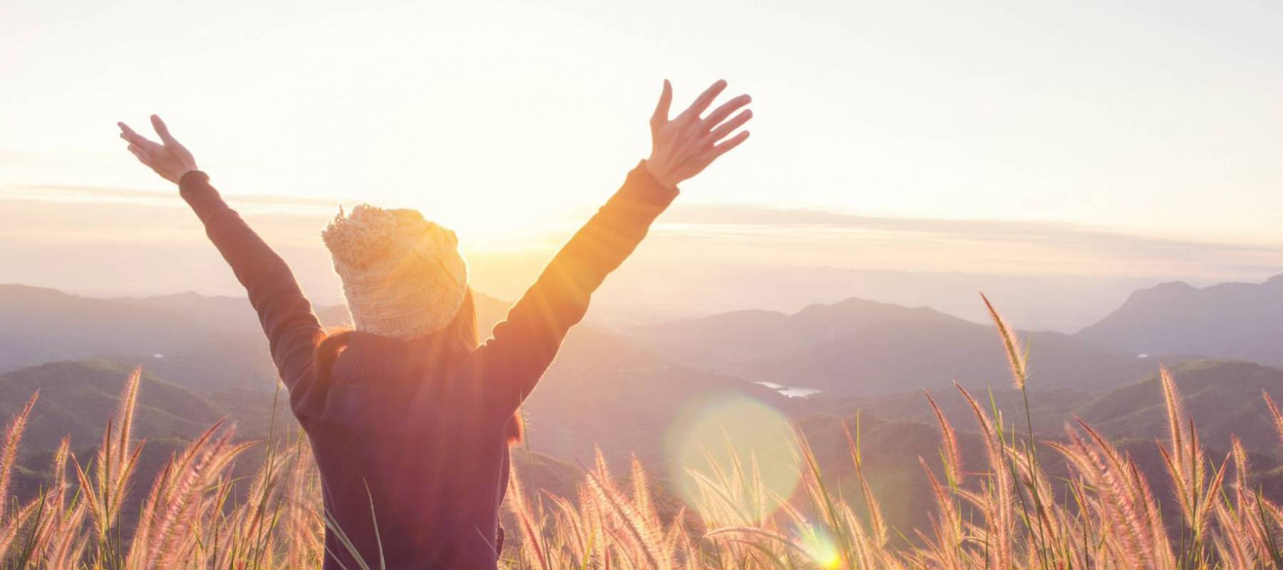 Carefree Happy Woman Enjoying Nature on grass meadow on top of mountain cliff with sunrise. Beauty Girl Outdoor. Freedom concept. Len flare effect. Sunbeams. Enjoyment.