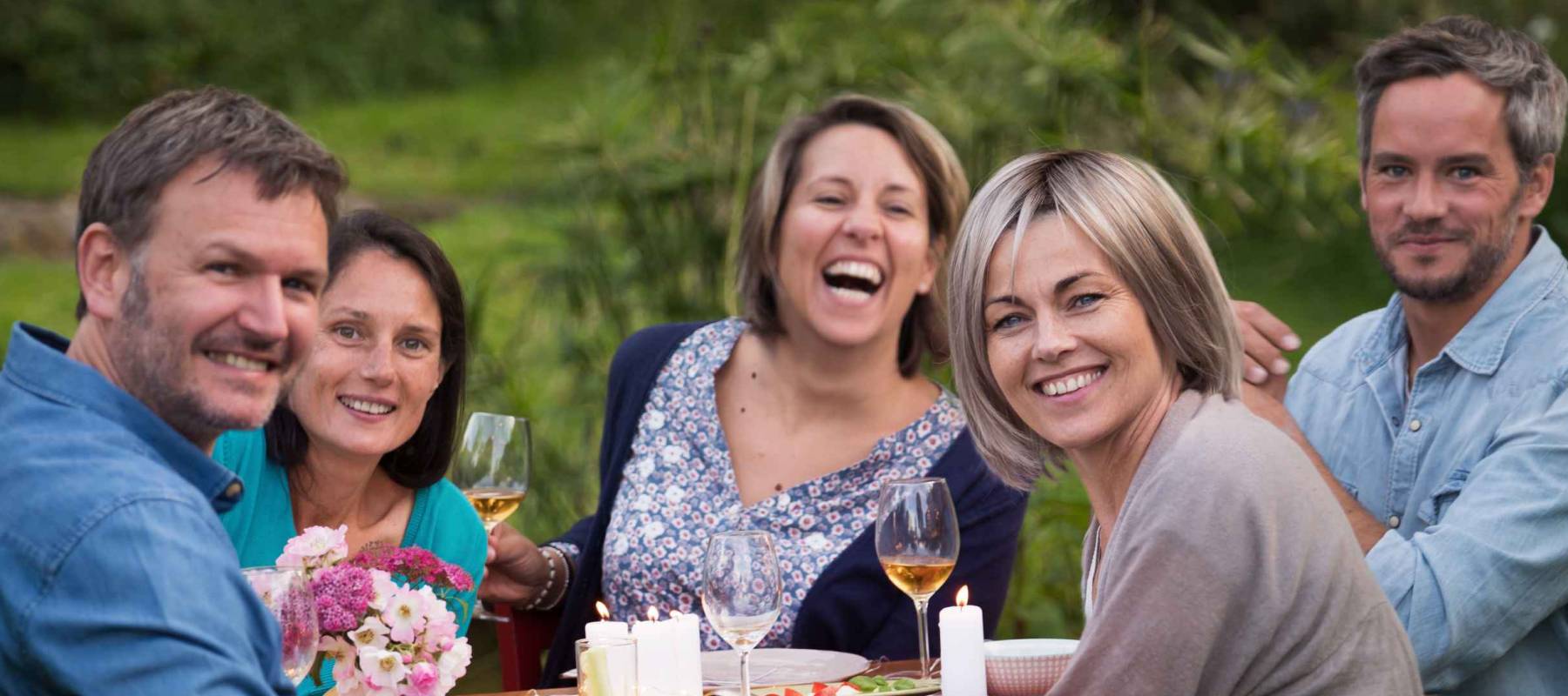 A summer evening of friends in their 40s gather around a table in the garden to share a meal and have fun together.
