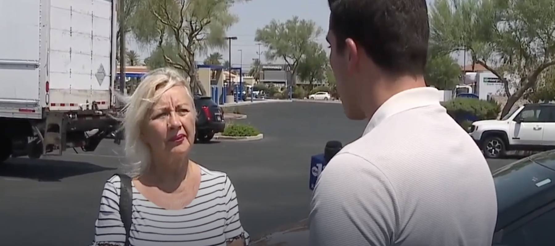 Reporter speaking to blonde woman in parking lot.