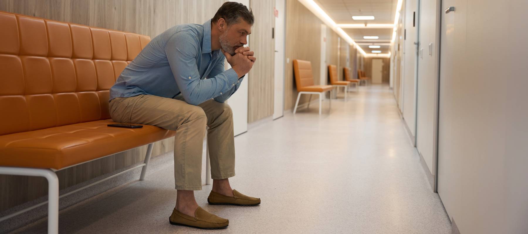 Late middle-aged man waiting in a hospital corridor.