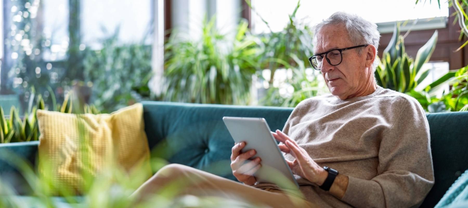 senior man using digital tablet while sitting on sofa in living room at home