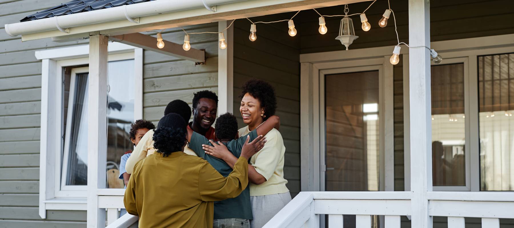 Portrait of happy black family embracing while standing on porch of new house, copy space