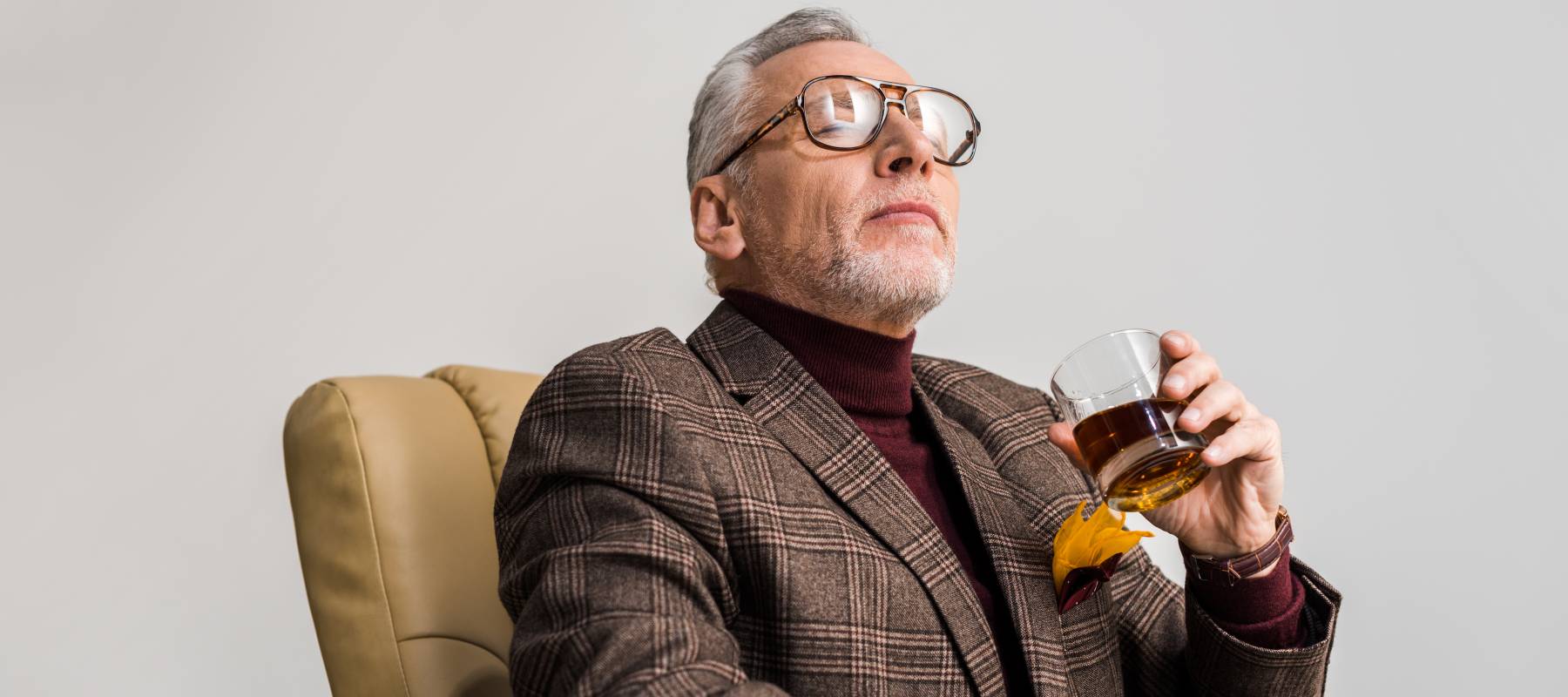 An aloof older gentleman enjoys a glass of whiskey as he contemplates how rich he is.