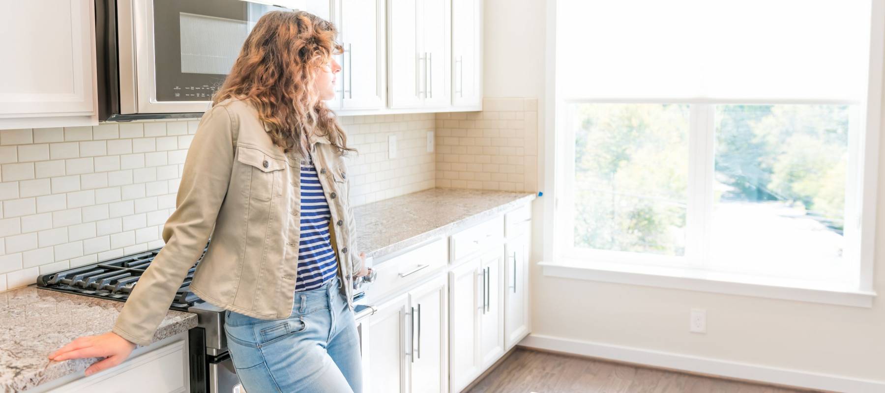 One young woman standing in kitchen in clean, modern, white home design before move-in