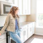 One young woman standing in kitchen in clean, modern, white home design before move-in