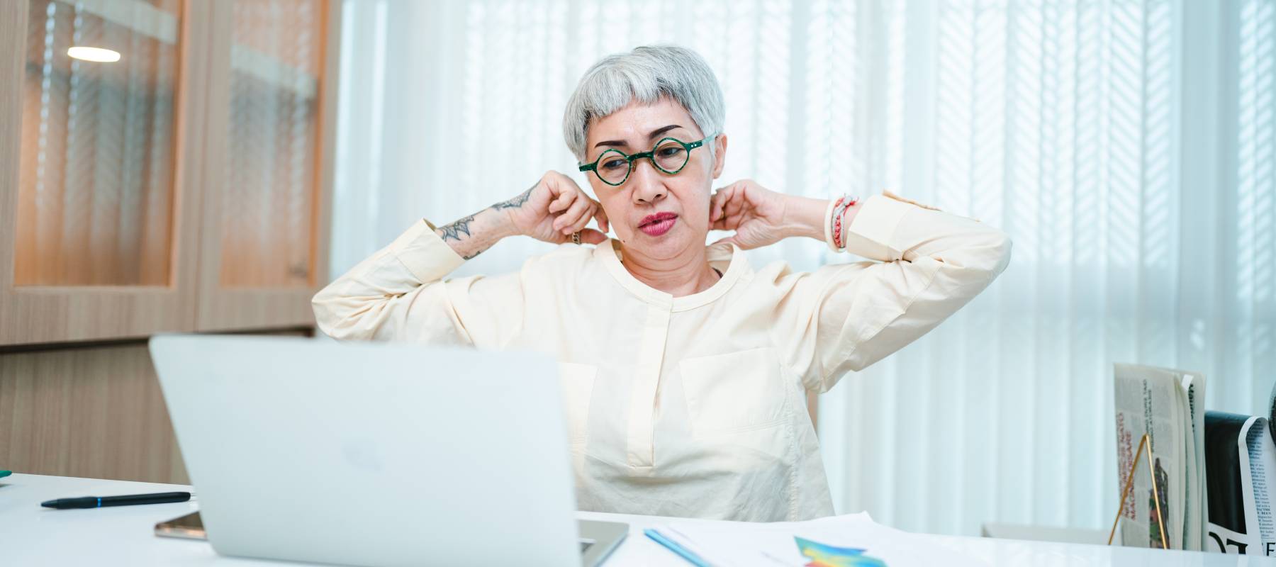 senior designer with grey hair wearing spectacles rubbing back neck while looking at laptop