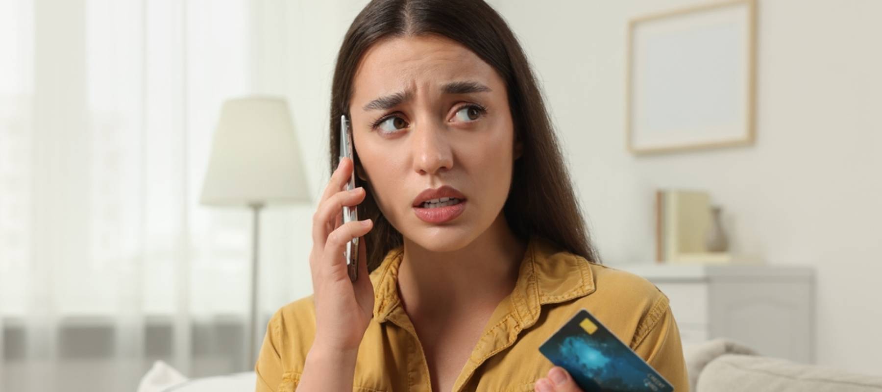 Confused woman with credit card talking on phone at home