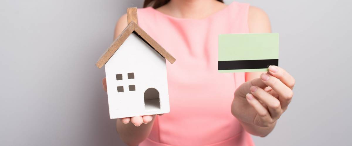 Invest in real estate concept. Woman holding small toy house and credit card in hands