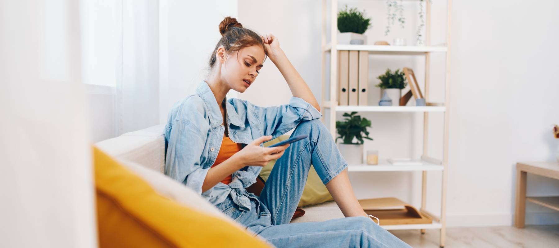 appy woman holding mobile phone and smiling while relaxing on cozy sofa at home