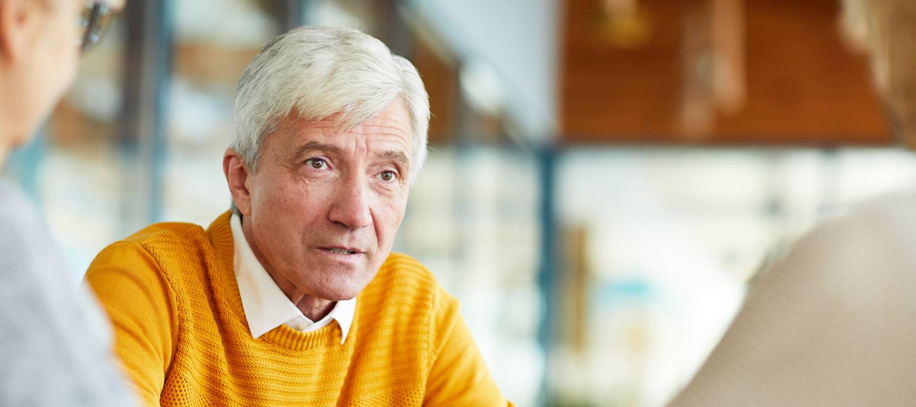 confident senior man with gray hair wearing yellow sweater talking to colleagues