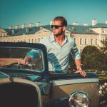 Confident wealthy young man with briefcase near classic convertible