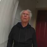 Man with white hair answers front door, looking surprised and concerned.
