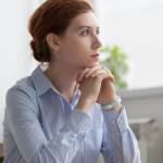 Lost in thoughts woman sits at workplace desk in office in front of laptop