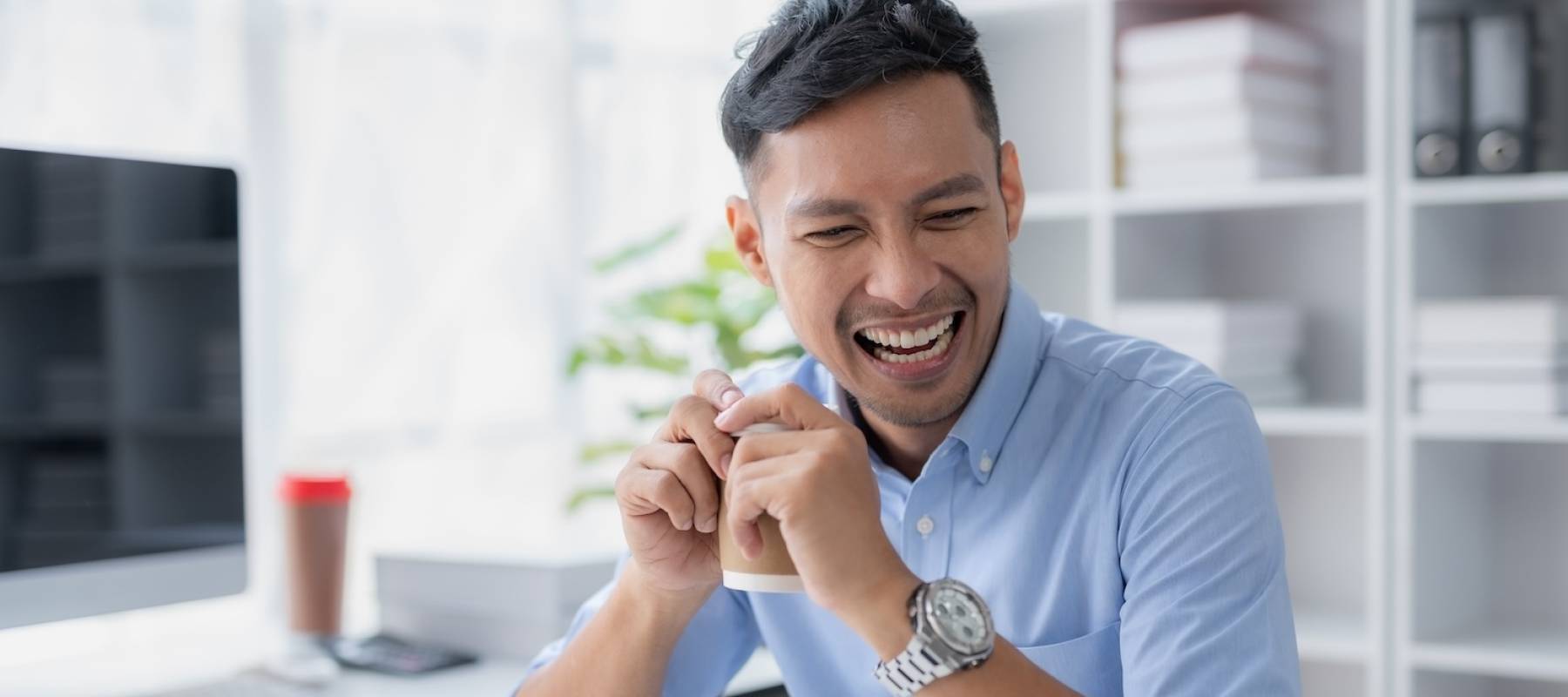 Happy smiling Asian businessman holding a coffee mug sitting happily in the office.