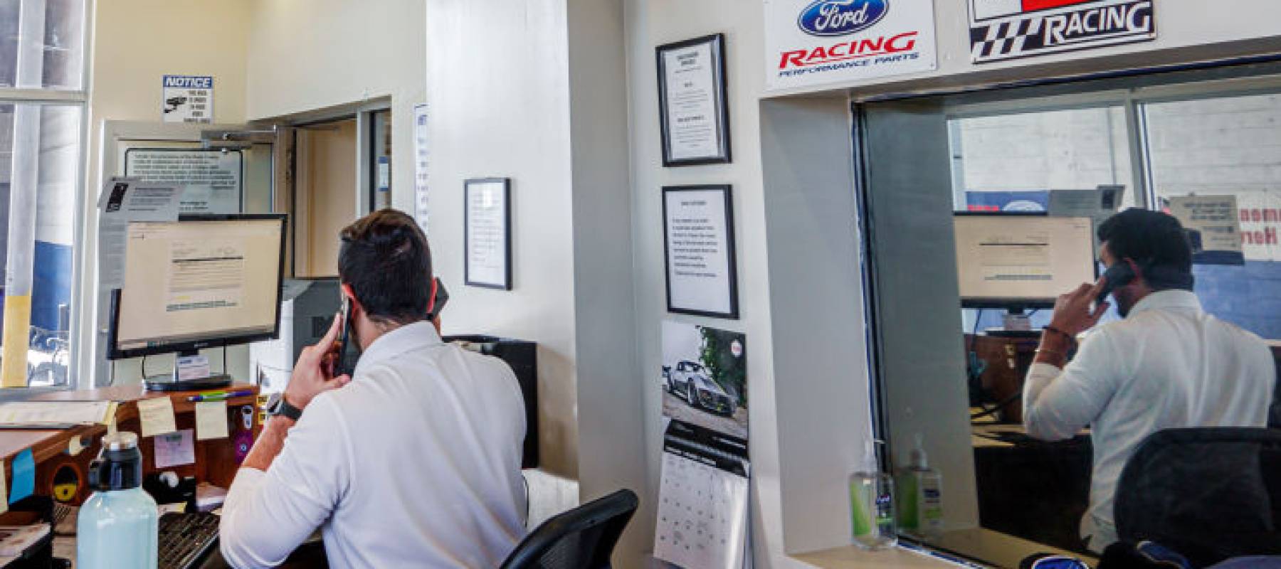 Ford car dealer service manager seen from behind, sitting at his desk on the phone.