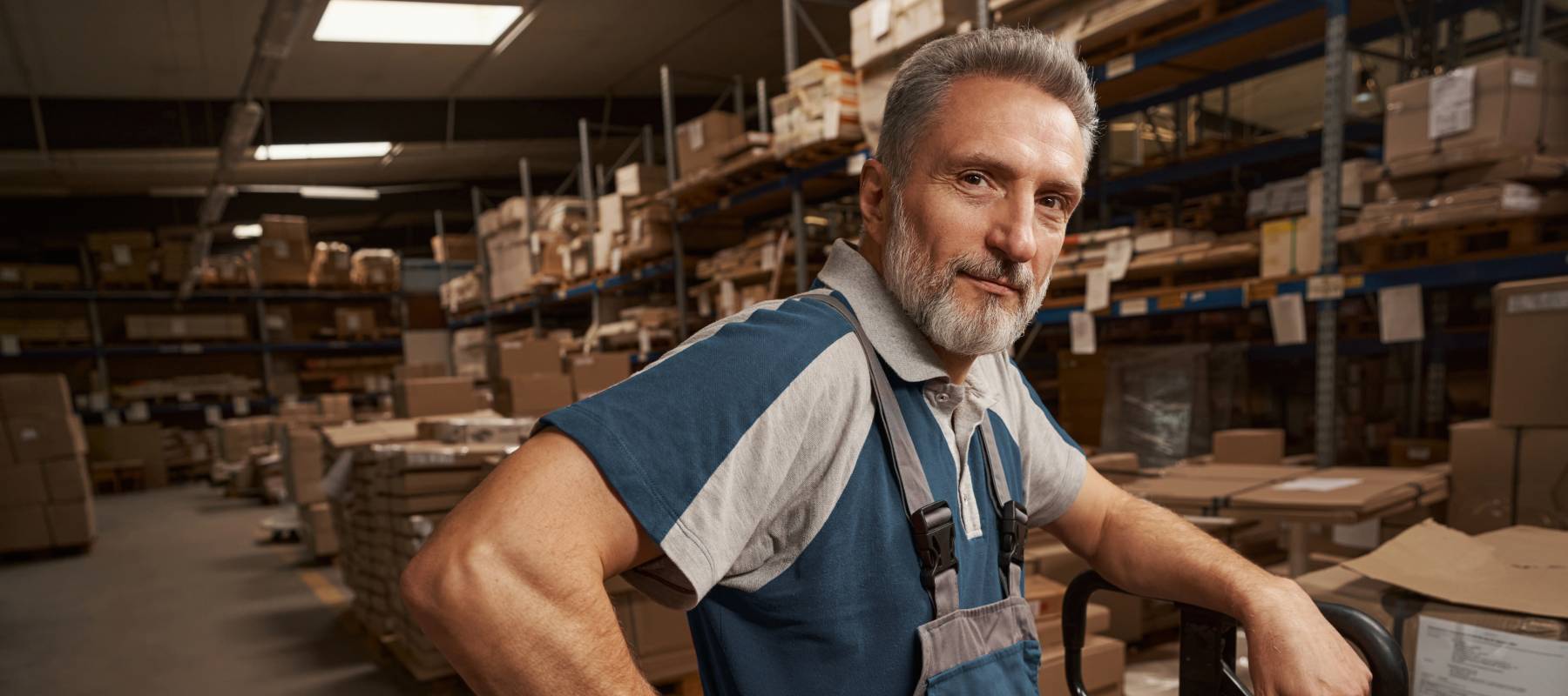 Happy older man looking directly at the camera, while working at a woodworking desk.