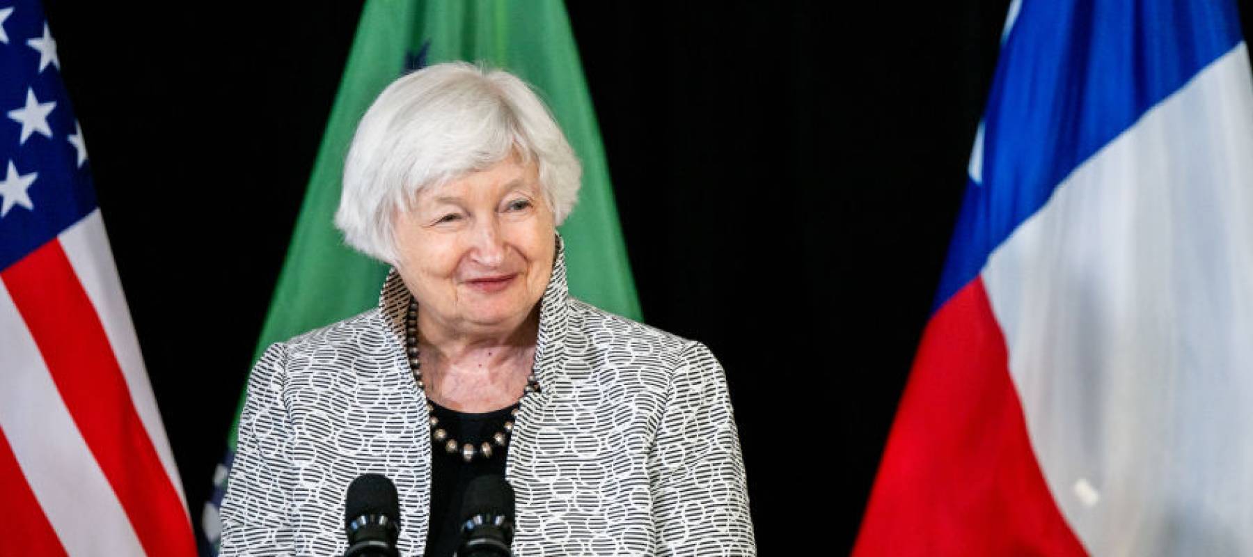 Janet Yellen smiles standing behind a podium on a stage at an IRS processing center.