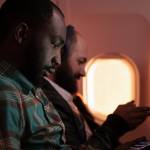 Businessmen work on their wireless devices during a flight.
