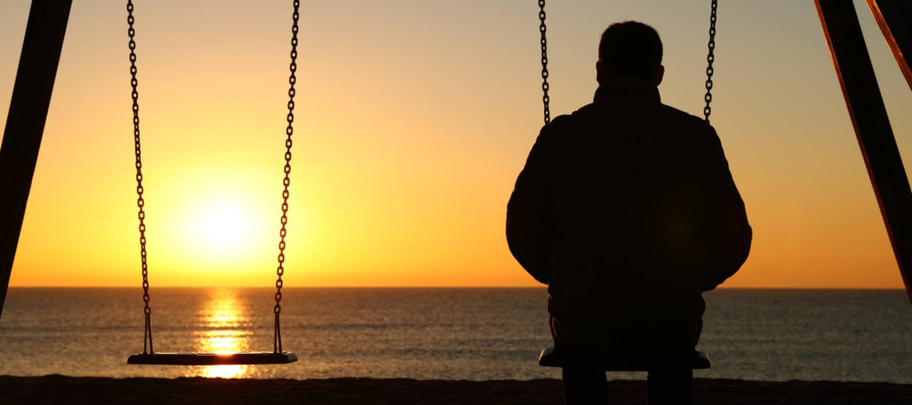 Back view backlighting silhouette of a man sitting on swing alone