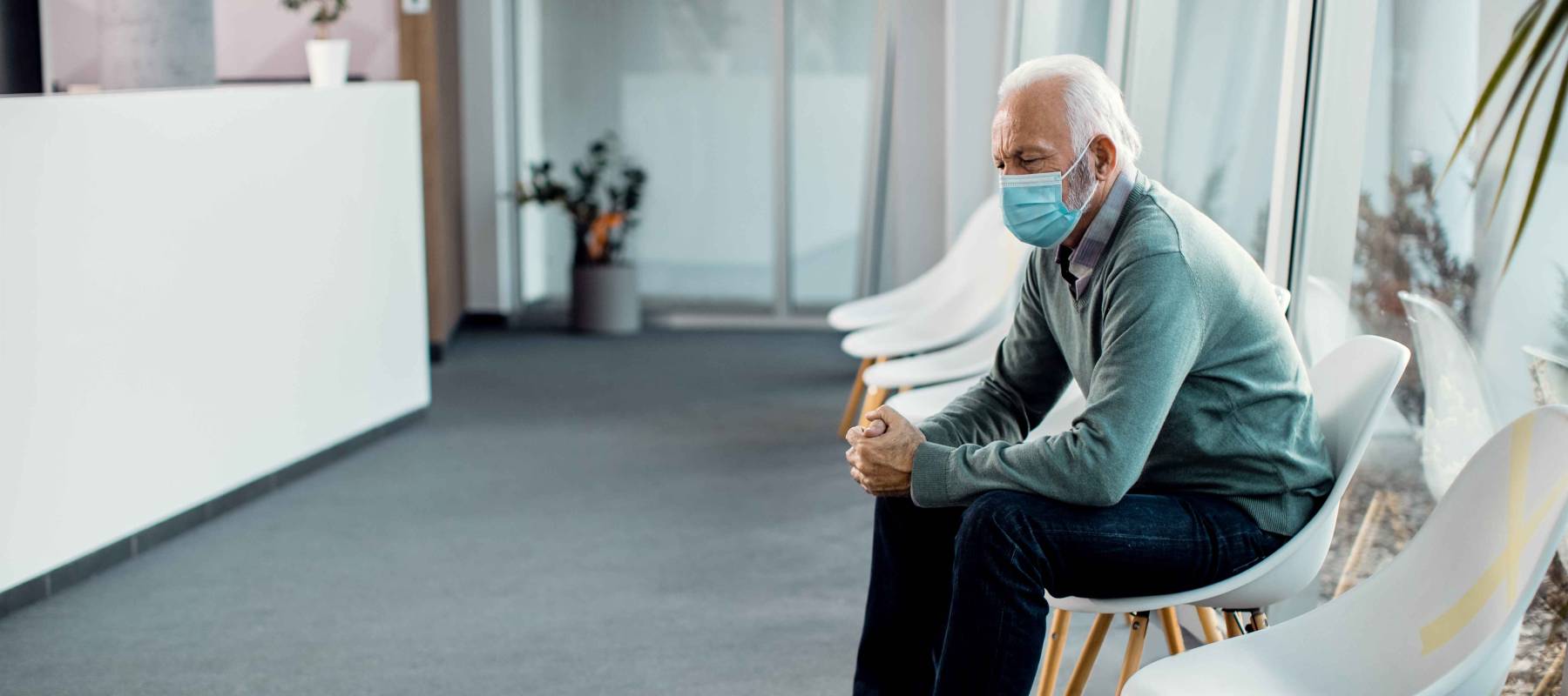 Caucasian senior man with protective face mask sitting in waiting room at the hospital