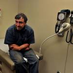 Man sits in doctor's office at end of examination table, looking uncomfortable and uncertain.