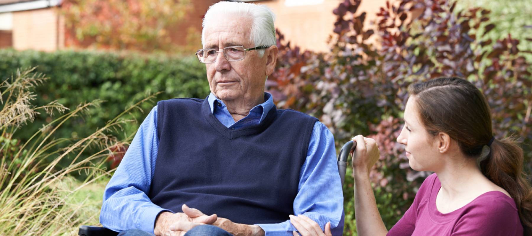 Adult Daughter Comforting Senior Father In Wheelchair