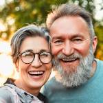 Mature, cheerful couple taking selfie portrait on phone.