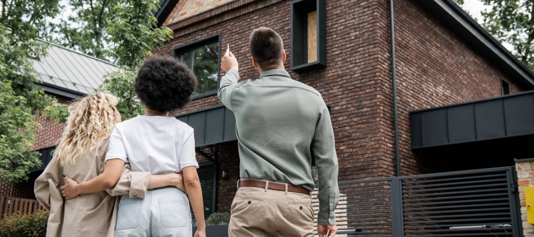 back view of real estate broker showing new cottage to interracial lesbian couple outdoors