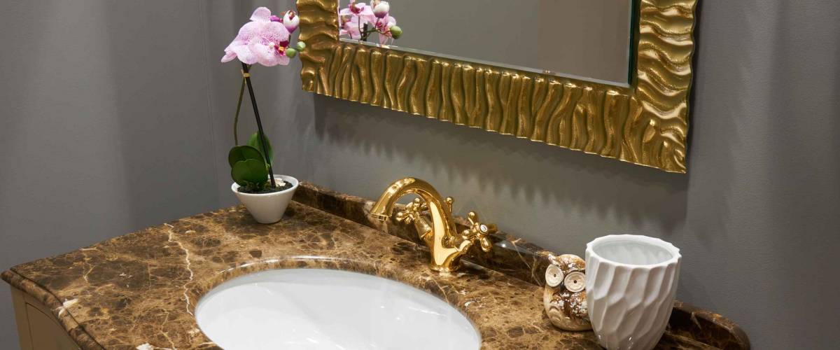 White inset ceramic washbasin in stone table, gold plated glossy metal mixer and a pair of towels