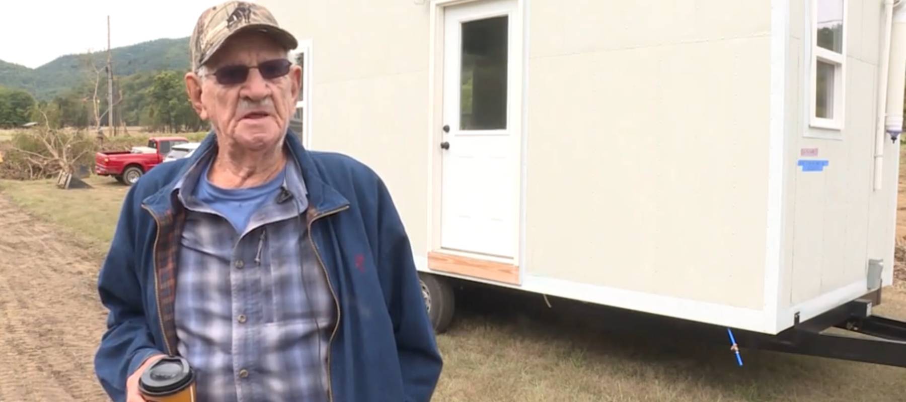Man stands holding a takeout coffee cup in front of a tiny home.