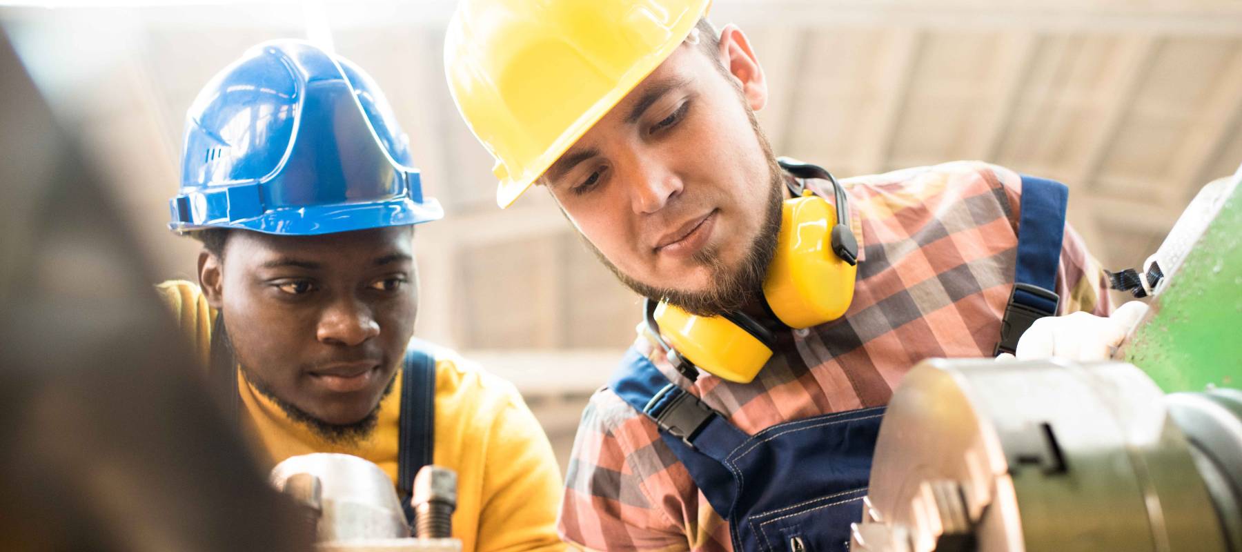 multi-ethnic team of lathe operators wearing overalls and hardhats gathered together at production department