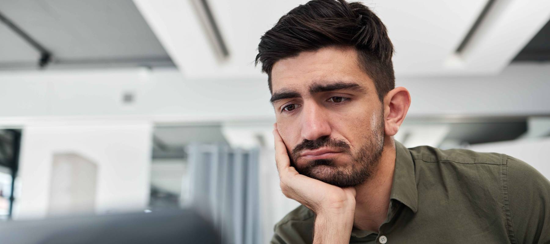 Man leans over, looking at laptop with chin in hand. Looking concerned.