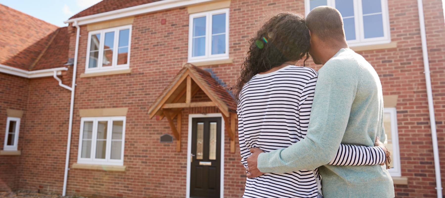 Rear View Of Couple Standing Outside New Home On Moving Day Looking At House