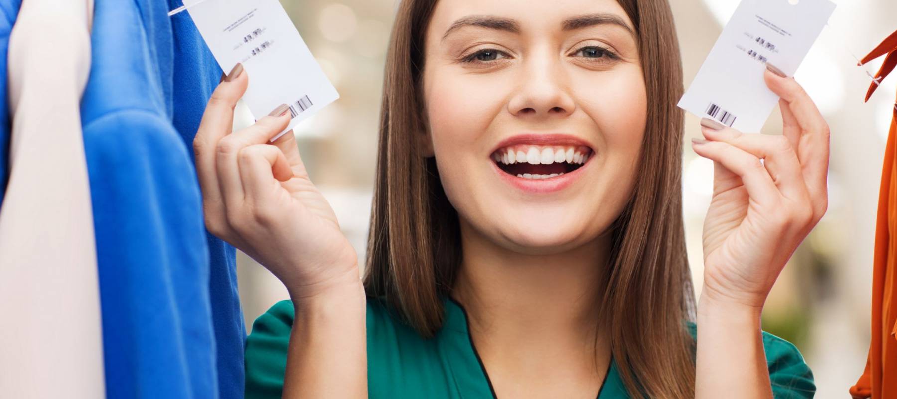 clothing, fashion, sale and people concept - happy woman showing price tags on clothes at shopping center or mall