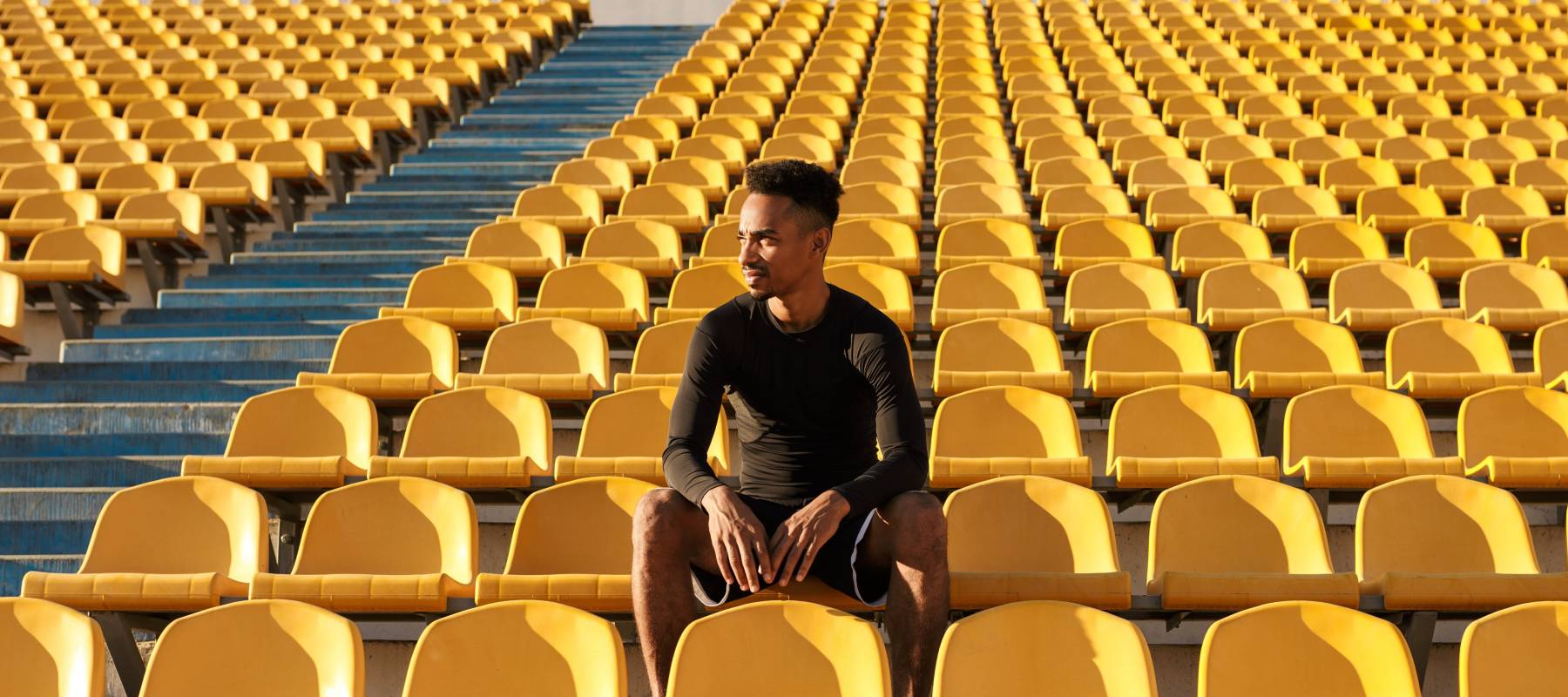 Young man sitting in sports stadium yellow seats, looking off to the side.