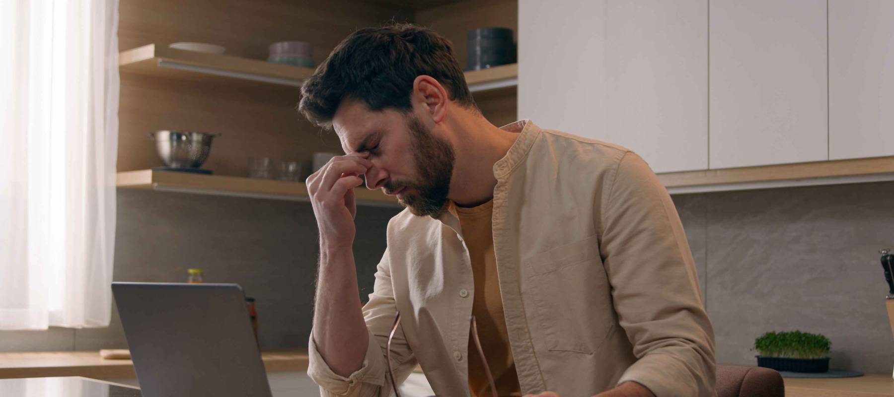 millennial Caucasian man working at home on a laptop, rubbing his eyes