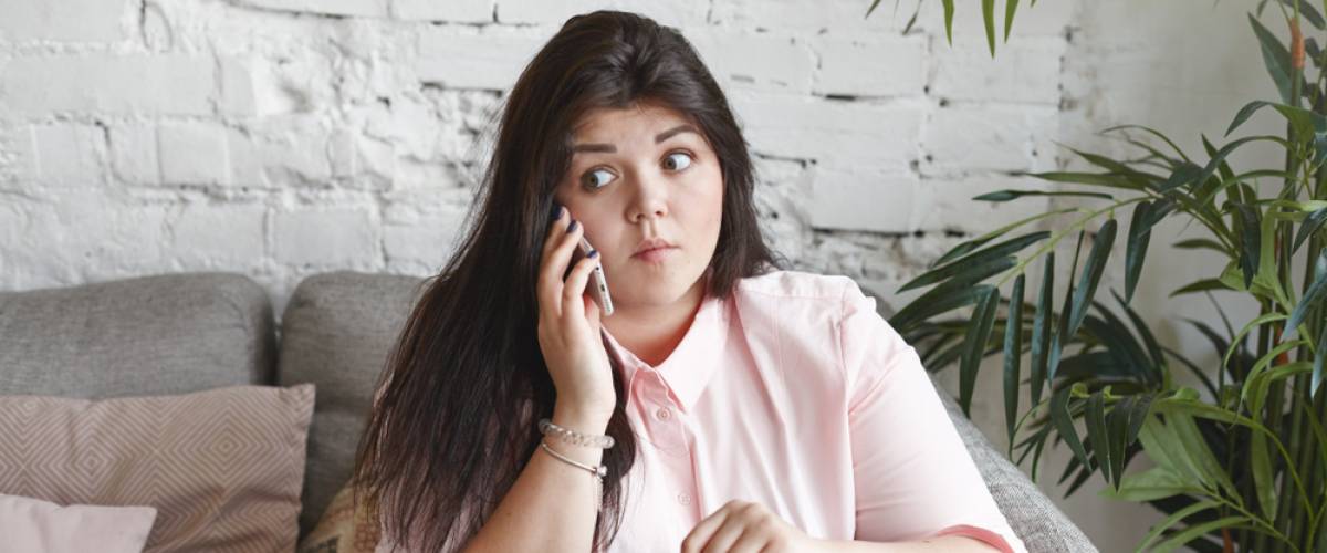 emotional young chubby woman having shocked surprised look on phone at home