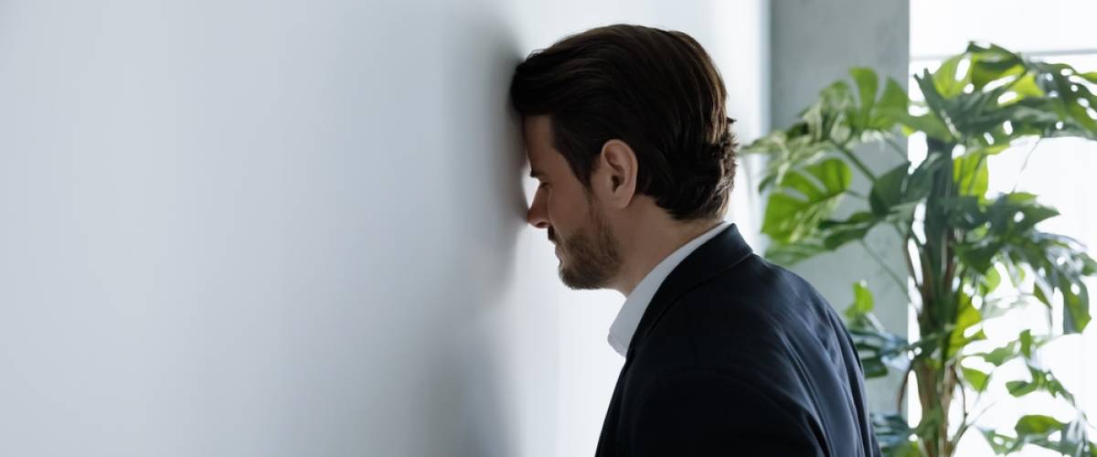upset businessman banging his head against wall in despair, looking stressed