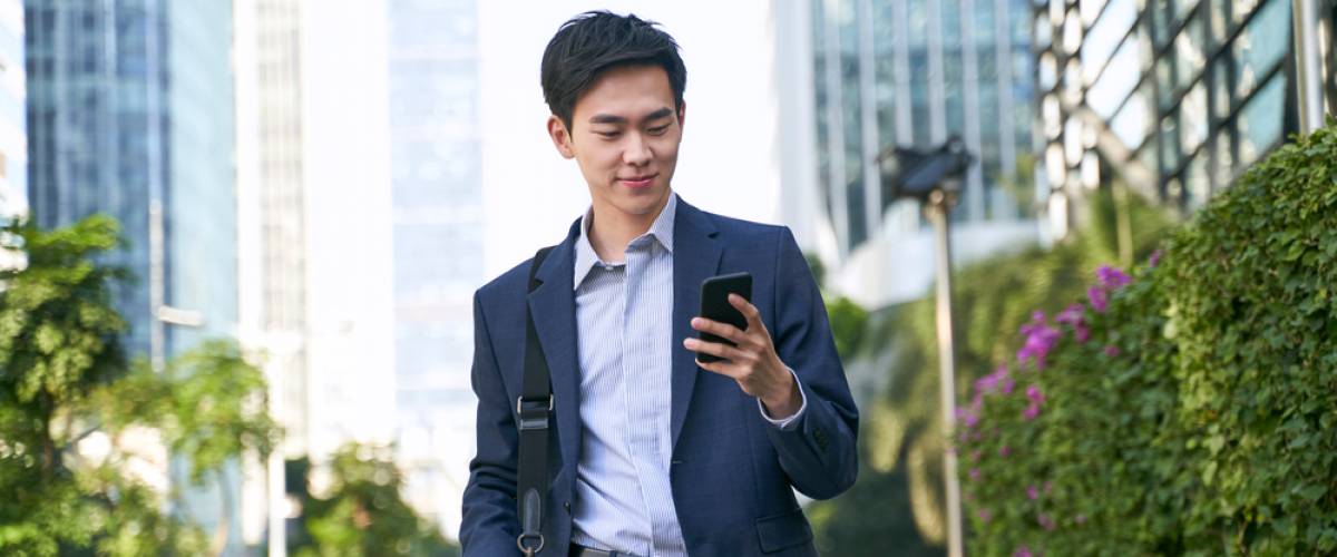 young Asian businessman looking at messages on phone while walking down street