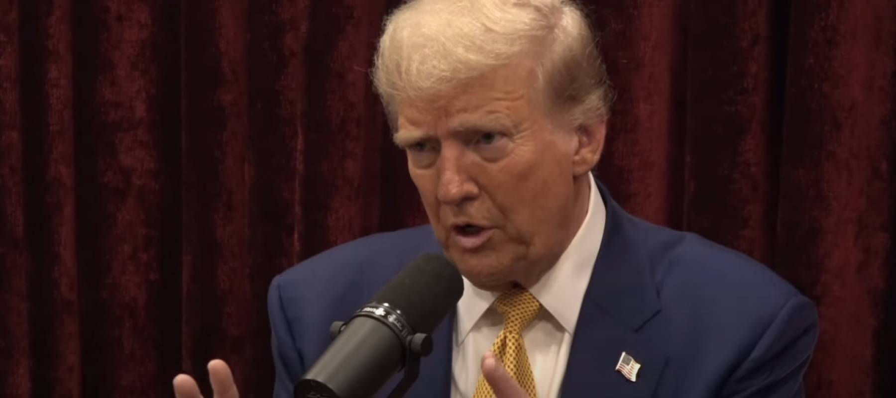 Donald Trump seen talking on set of the Joe Rogan Experience podcast, gesturing with his hands.