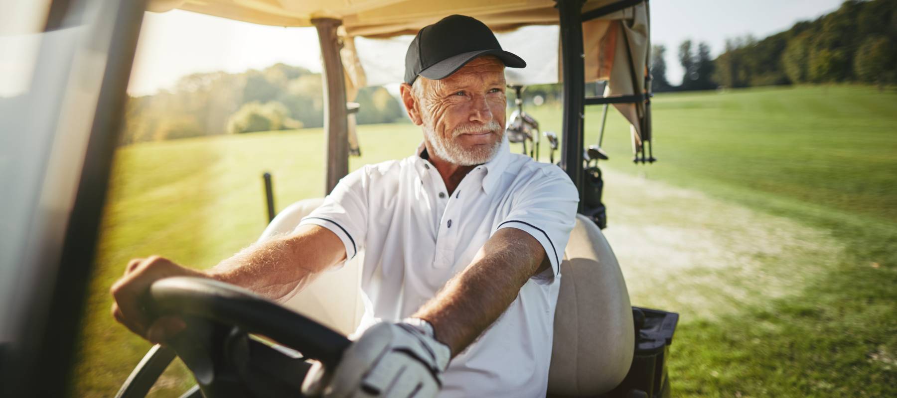A mature man sitting in a golf cart looking off to the side.